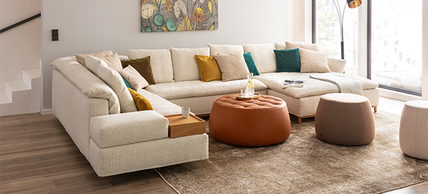 Modulares Ecksofa Isla von Signet mit Schlaffunktion. Modulares Ecksofa Isla von Signet mit Schlaffunktion, abgebildet in einem modernen Wohnzimmer mit dekorativen Hockern und Lederhocker.