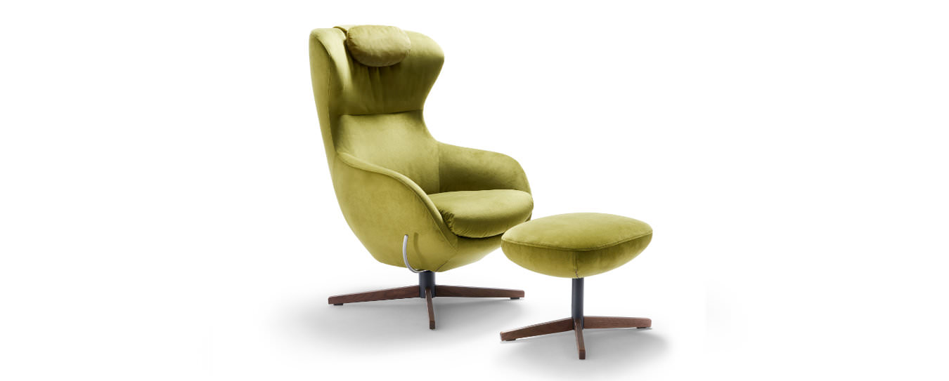 Der Sessel Jester von Signet mit dem gruenen Velourstoff Milan, einem Nussbaumholzgestell und einem Hocker. Sessel Jester Signet Velourstoff Milan gruen Holzgestell Nussbaum